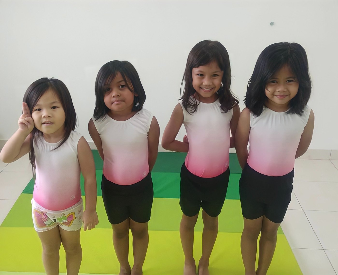 Four young students in matching gymnastics tops smiling at the camera.