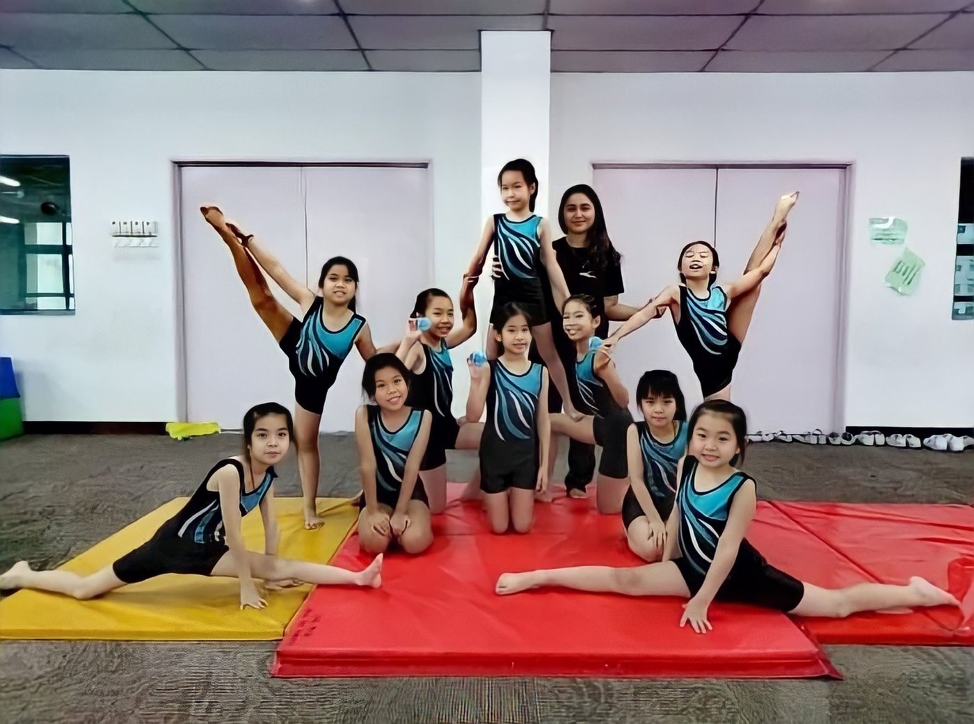 Young gymnasts practising balance and flexibility together on red and yellow mats, with their coach.