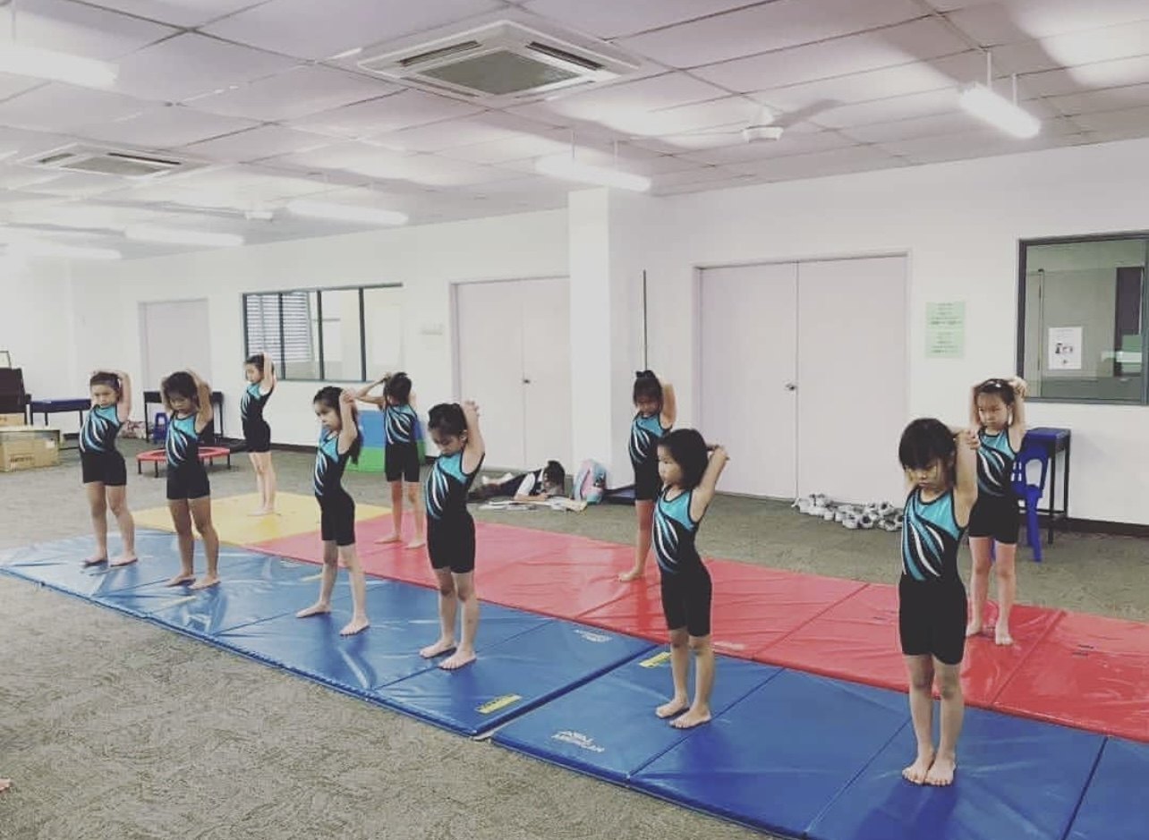 Children in a gymnastics class practising standing arm stretches.
